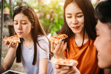 Asian students eating eating the pizza together in breaking time early next study class having fun and enjoy party, Italian food slice with cheese delicious at university outdoor.
