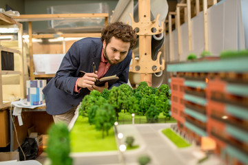 Young man with pen and notebook making working notes while looking at new park on city layout