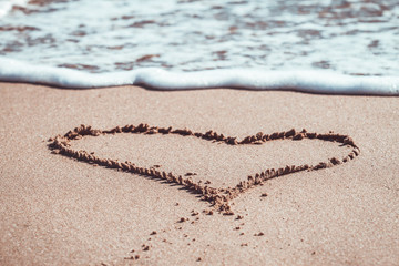 Heart drawn on the sand of the beach and blue sea waves with foam