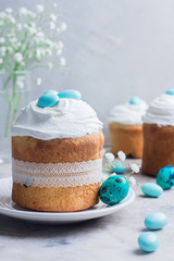 Easter cake kulich. Traditional Easter sweet bread decorated meringue and blue candy cane shape eggs on plate on gray stone table background. Copy space.