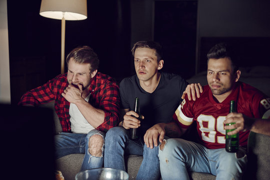 Men friends watching american football in the evening.
