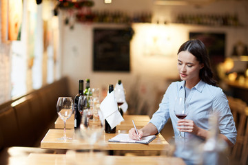 Young female sommelier making notes while tasting different sorts of wine