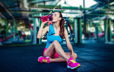 Fototapeta na wymiar Healthy lifestyle. Attractive young smiling sportswoman in sport wear drinks water in the gym.