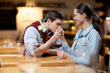 Young romantic man kissing hand of his girlfriend in cafe and going to give her white rose