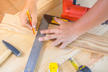 The carpenter uses a pencil on the wooden board in workshop.