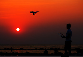 Man operating of flying drone quadrocopter at sunset