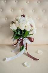 a wedding bouquet of white roses on a yellow background of a leather sofa with two years and rose petals