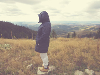 Woman on a cold mountain top with landscape in the background.