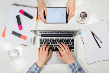 Modern workplace top view. male and female hands working with tablet and laptop pc at modern white workplace desktop together on financial, business or school activity.