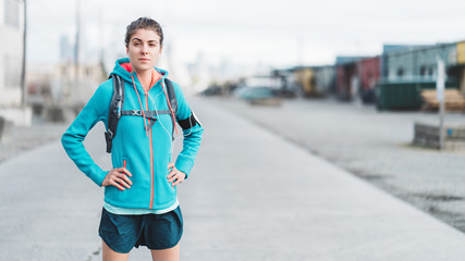 Portrait of young sporty woman with running backpack and listening music in urban zone