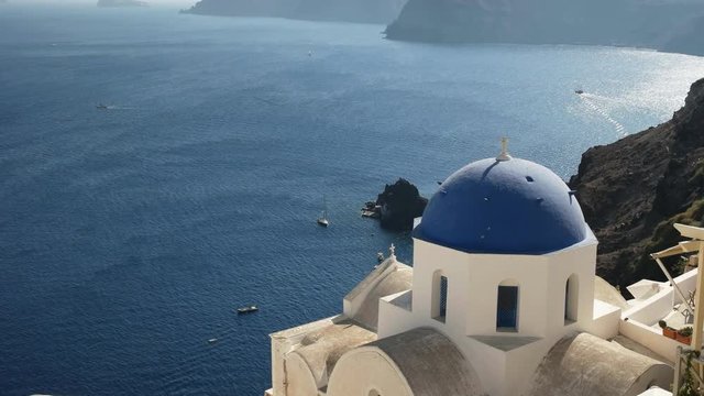 high angle pan of a blue domed church and the blue aegean sea at oia on the island of santorini, greece