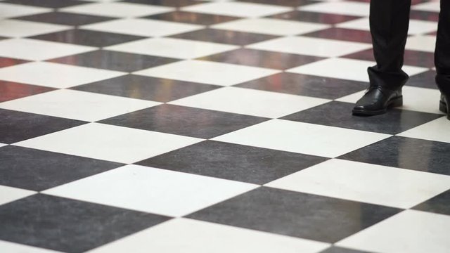quirky and retro black and white tile floor. A crowd of people gathers a gallery. people wear different footwear walking the floor. lonely man waiting for someone