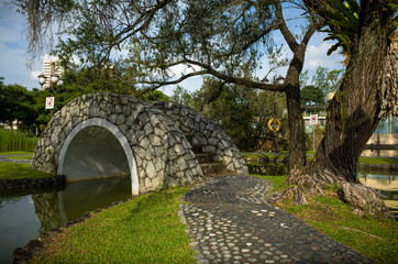 Fototapeta na wymiar A stone Bridge at Toa Payoh Town Park provides a walkway over a pond.