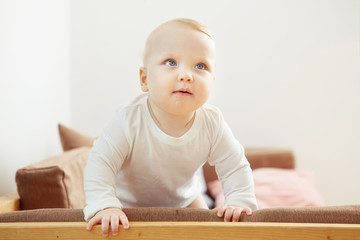 Smiling baby standing at the sofa relying on support.