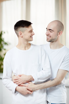 Young gay partners in white T-shirts looking at one another in embrace