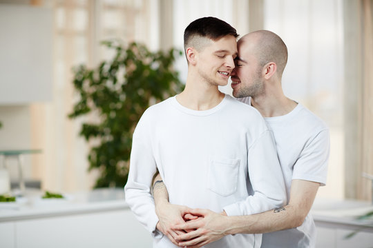 Amorous gay men standing in embrace with their eyes closed and smiling