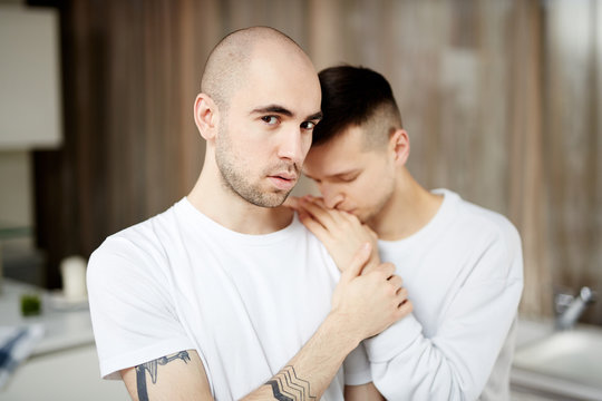 Young gay man looking at camera with his desperate partner head on his shoulder
