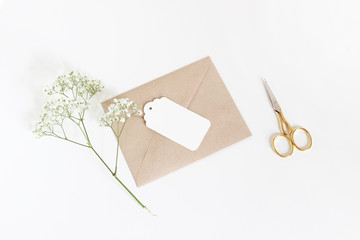 White gift tag with craft paper envelope, golden scissors and baby's breath Gypsophila flowers...