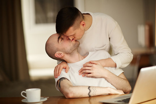 Two young gay men sharing passionate kiss while spending time at home together