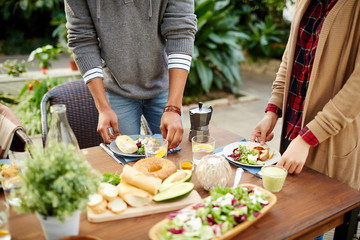 Two people putting vegetarian self-made food on dinner table