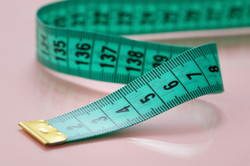 Close-up of green measuring tape on pink background.