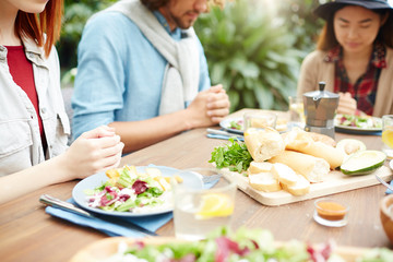 Served table with homemade food and hands of several friends praying before dinner
