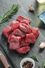Close-up of chopped raw beef meat with fresh rosemary and spices on black table.