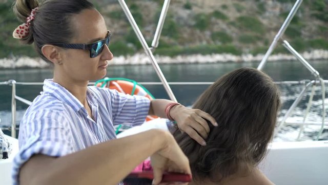 Family sailing boat on sea, woman brushing her daughter's hair
