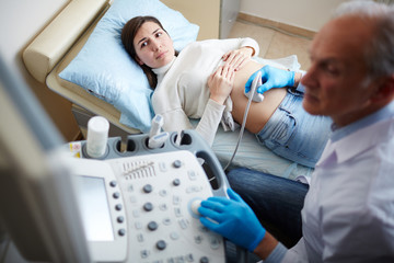 Pregnant woman looking at screen of ultrasound equipment during regular examination