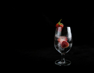 Sparkling water with strawberry in a high glass on black background.