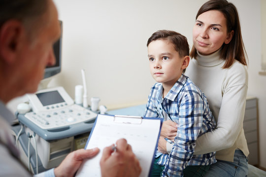 Young woman and her little son looking at doctor and listening to his advice during appointment