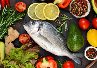 Food background. Fresh, raw Dorado with a swallow, lemon, avocado on a dark concrete background.