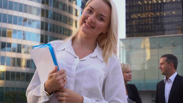 Close up face secretary looking at camera with document case in slow motion and partners background.