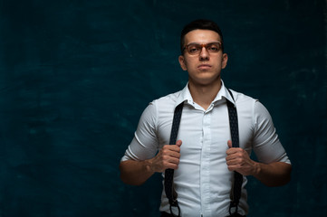 Portrait of confident young business man in formal suit with suspenders on dark blue grunge background. Copyspace