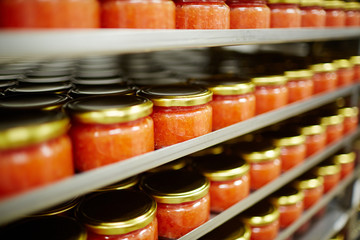 Salted red caviar in small jars standing on shelves in seafood producing plant