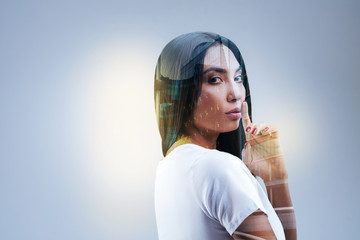 City lights. Elegant creative free woman  putting finger near lips while posing on the  grey...