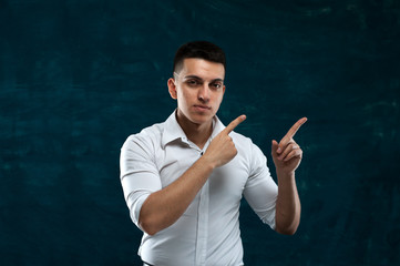 Close-up portrait of positive young man in white shirt showing something useful on dark blue background