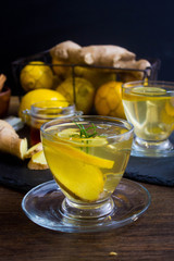 Glass cup of hot tea with mint, honey, ginger and lemon on dark background.