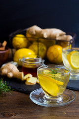 Glass cup of hot tea with mint, honey, ginger and lemon on dark background.
