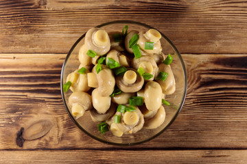 Glass bowl with pickled champignons. Marinated mushrooms on wooden table