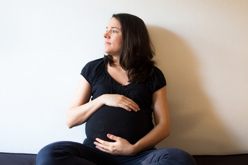 Young expecting female sitting at home on a couch and touching her belly