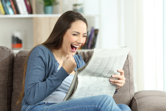 Excited woman reading a newspaper on a couch