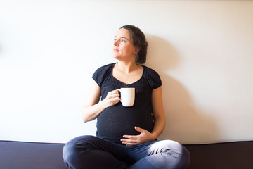 Young expecting female sitting at home on a couch and touching her belly