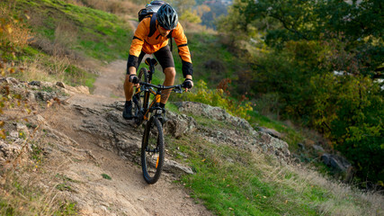 Obraz na płótnie Canvas Cyclist in Orange Riding the Mountain Bike on the Autumn Rocky Trail. Extreme Sport and Enduro Biking Concept.