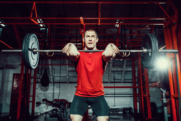 Muscular fitness man doing deadlift a barbell over his head in modern fitness center. Functional...