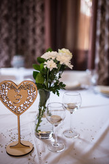 Wedding decoration: candles in glasses, white flowers in vase. Wedding wooden table numbers in a shape of a heart.