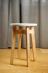 Wooden stool with round seat and long legs stands on parquet floor