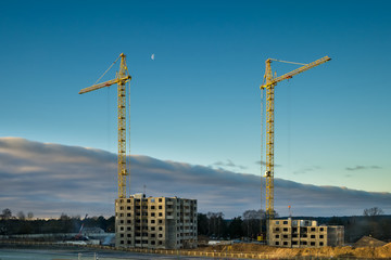 Silhouette tower cranes and unfinished multi-storey high buildings under construction in cloudy day with moon