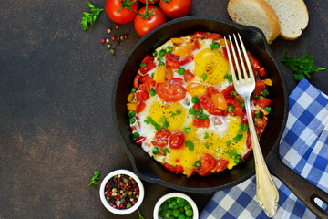 Eggs with tomatoes, pepper and green peas in a frying pan on a concrete background.