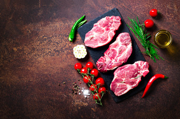 Raw meat, beef steak on a stone cutting board with rosemary, spices, salt, oil, cherry tomatoes, hot pepper and herbs